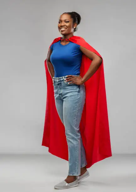 women's power and people concept - happy african american woman in red superhero cape over grey background