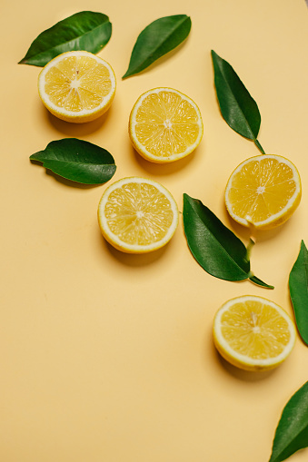 Slices of fresh lemon and lemon leaves on yellow background with copy space