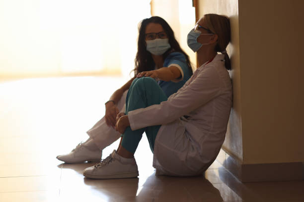 mujeres cansadas doctoras están sentadas en máscaras en pasillo - doctor tired protective workwear sadness fotografías e imágenes de stock