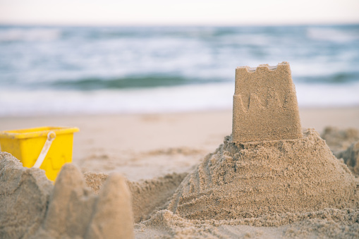 Photo of a Sand castle made on a ocean beach next to the sea with a Yellow Beach Bucket toy visible