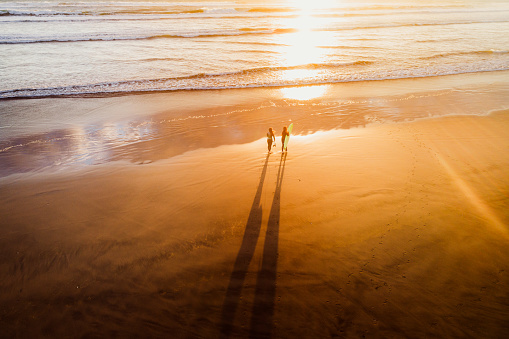 Two women carrying surfboard on beach at sunset time.
