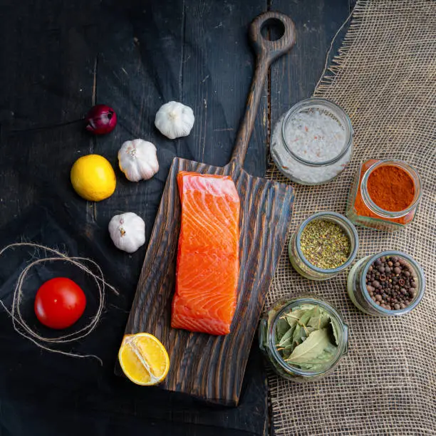 Photo of A piece of cold-smoked salmon on a serving board. Vegetables and seasonings for fish