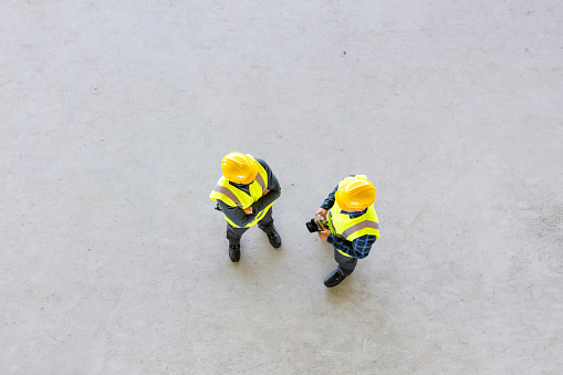 High angle view of builders wearing work helmets and reflective vest standing on concrete floor and discussing.