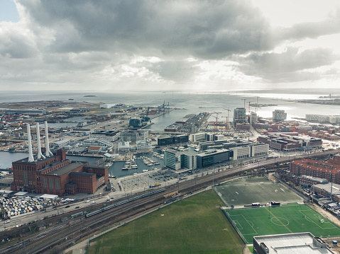 Electric city train running on rails next to the car traffic in in Copenhagen, Denmark. Aerial view shot with drone in the up-class Nordhavn area. Public transportation by train and bus are together with bicycling the fastest way to to get to work in this capital. The sustainable electric train contrasts the natural gas fired power station, Svanemølle Værket.