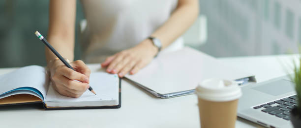 istock Close up view of young female hand with pencil writing on notebook while doing homework 1311065631
