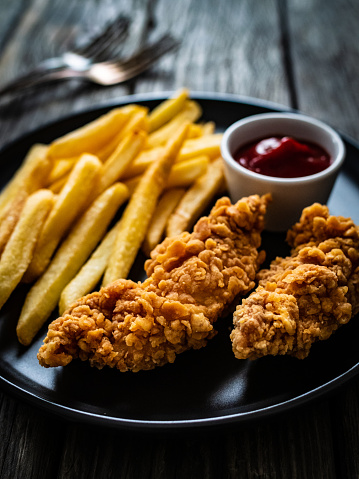 Fried chicken nuggets with French fries and ketchup on wooden table