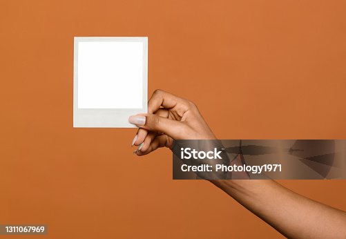 istock Black female hand holding up a blank instant photo frame 1311067969