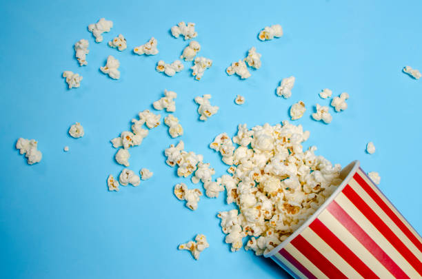 popcorn spilled from a paper bucket delicious popcorn spilled from a paper bucket on a blue background popcorn stock pictures, royalty-free photos & images