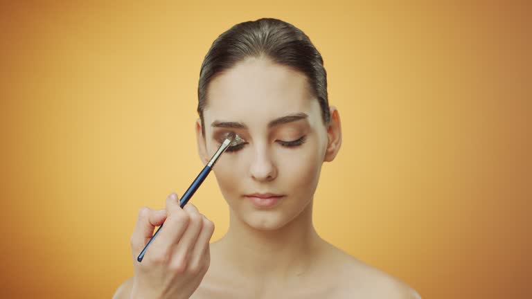 Steps of make-up applying. Make-up artist applies glitter cream eyeshadow to the eyelid of a brunette girl with a make-up brush.