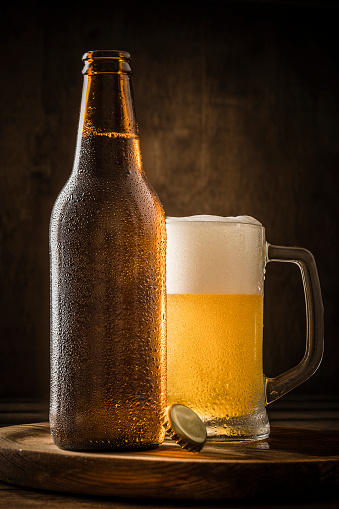 Front view of a beer bottle with a drinking glass full of beer on a rustic wooden table. Low key DSLR photo taken with Canon EOS 6D Mark II and Canon EF 100 mm f/ 2.8