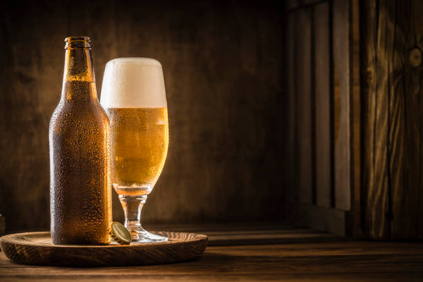 bottiglia di birra con bicchiere da bere pieno di birra su un tavolo rustico in legno - birra foto e immagini stock