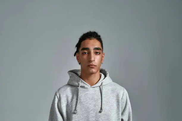Handsome young gypsy man in hoodie looking at camera while posing on light background. Stop racism concept