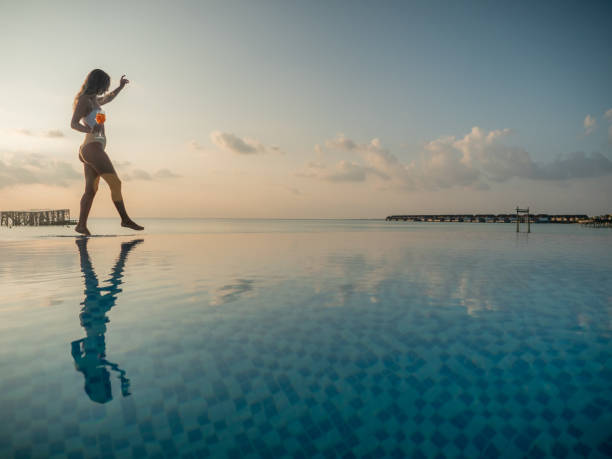 woman walking at the edge of infinity pool at sunset - swimming pool resort swimming pool poolside sea imagens e fotografias de stock