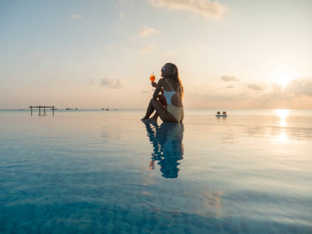istock Woman drinking cocktail at sunset in an infinity pool 1311070095