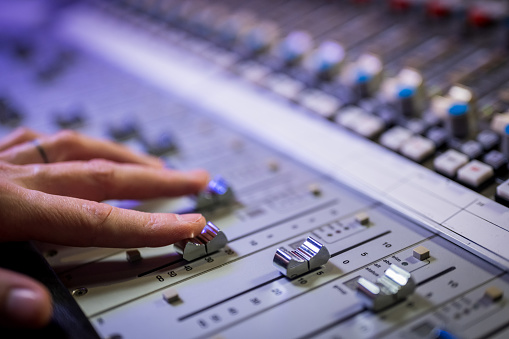 Close-up of man's hand adjusting buttons on audio mixer in recording studio.