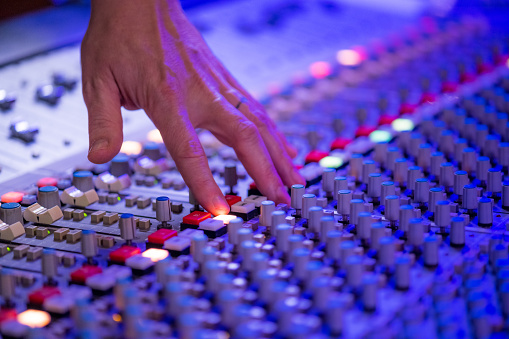 Close-up of man's hand adjusting buttons on audio mixer in recording studio.