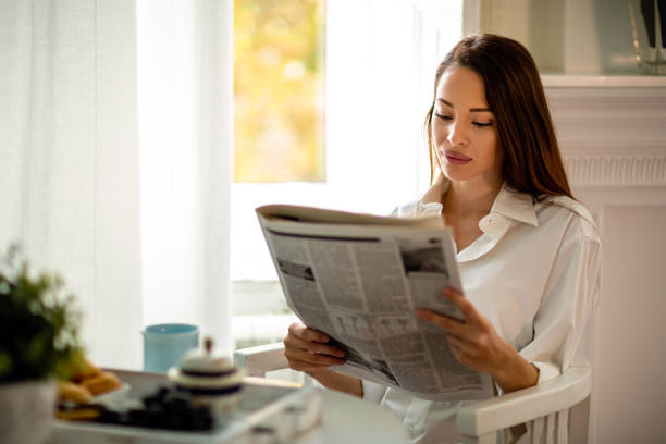 istock Young woman reading newspaper while having morning coffee at home 1311073210