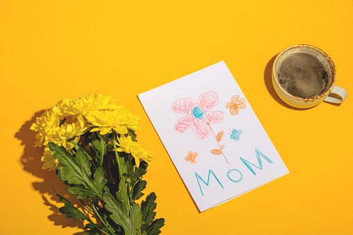 A gift from a child for mothers day - a card from a picture and coffee with flowers in the morning. High quality photo. Top view