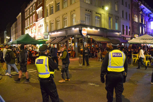 Police and crowd of people in Soho, London, at night London, United Kingdom - November 4 2020.Police officers and crowd of people on Old Compton Street, Soho at night. Temporary al fresco street seating was implemented to allow bars and restaurants to operate and facilitate social distancing during the coronavirus pandemic. covent garden photos stock pictures, royalty-free photos & images