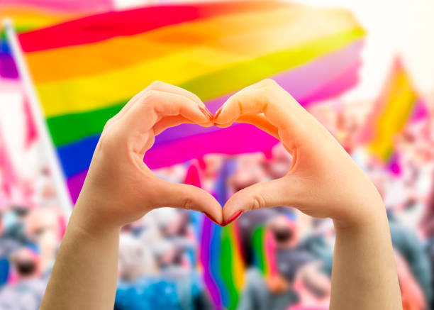 hands make heart shape in a gay pride parade Supporting hands make heart sign and wave in front of a rainbow flag flying on the sidelines of a summer gay pride parade honor concept stock pictures, royalty-free photos & images