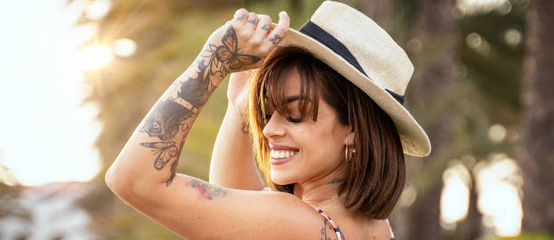 joven hermosa mujer morena feliz con sombrero de verano, sonriendo encantadoramente. chica con tatuajes. - flequillo fotografías e imágenes de stock