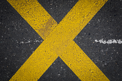 Yellow crossing lines, like a x on a dark grey asphalt, space for text, no person