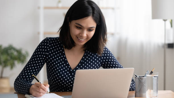 istock Asian female student watch tele lecture on pc make notes 1311084726