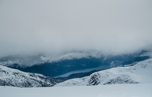 Abstract view of fjord surrounded by snowy mountains and clouds in Sunnmore, Norway.