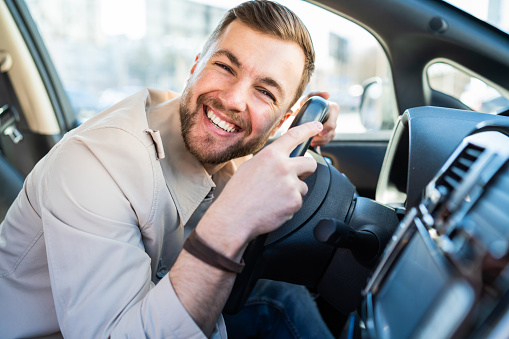 Satisfied man loves his car. Positive driver lies on the steering wheel of the auto