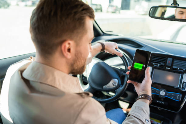 istock Man watching electric car charge indicator through smartphone app. Battery level on the mobile phone screen 1311086677