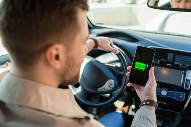 istock Man watching electric car charge indicator through smartphone app. Battery level on the mobile phone screen 1311086709