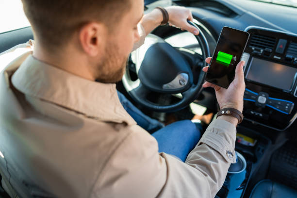 istock Man watching electric car charge indicator through smartphone app. Battery level on the mobile phone screen 1311086772