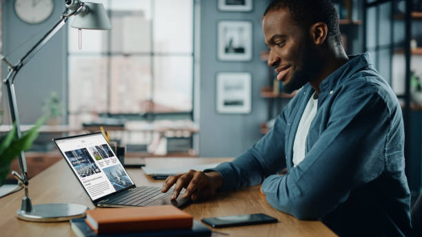 istock Handsome Black African American Specialist Working on Laptop Computer in Creative Home Living Room. Freelance Male is Reading News for Financial Market Analysis and Report for Clients and Employer. 1311088134