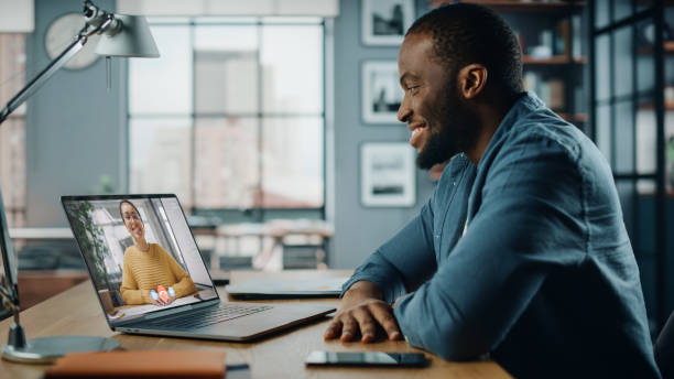 istock Handsome African American Man Having a Video Call on Laptop Computer while Sitting Behind Desk in Living Room. Freelancer Working From Home and Talking to Colleagues and Clients Over the Internet. 1311088154