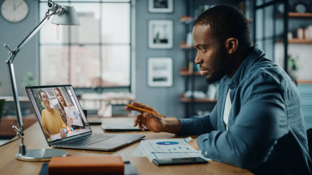 istock Handsome African American Man Having a Video Call on Laptop Computer while Sitting Behind Desk in Living Room. Freelancer Working From Home and Talking to Colleagues and Clients Over the Internet. 1311088172