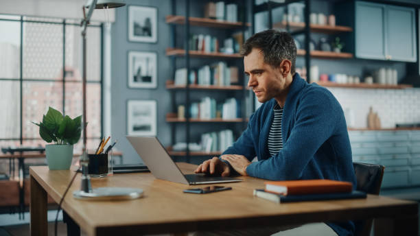istock Handsome Caucasian Man Working on Laptop Computer while Sitting Behind Desk in Cozy Living Room. Freelancer Working From Home. Browsing Internet, Using Social Networks, Having Fun in Flat. 1311088205