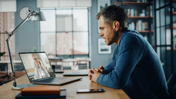 istock Handsome Caucasian Man Having a Video Call with Female Doctor on Laptop Computer while Sitting Behind Desk in Living Room. Freelancer Working From Home and Talking a Medic Over the Internet. 1311088210