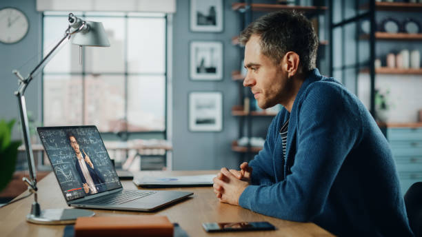 istock Handsome Caucasian Man Having an Online Video Lesson on Laptop Computer while Sitting Behind Desk in Living Room. Freelancer Working on His Skills or Student Doing Homework Over the Internet. 1311088224