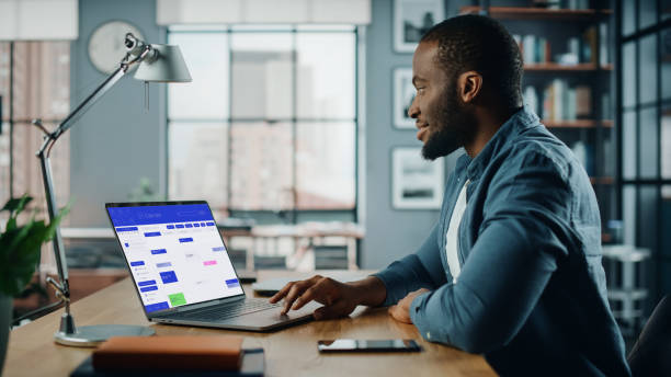 istock Handsome Black African American Specialist Working on Desktop Computer in Creative Home Living Room. Freelance Male is Checking His Calendar to Make an Appointment with New Clients and Employer. 1311088251