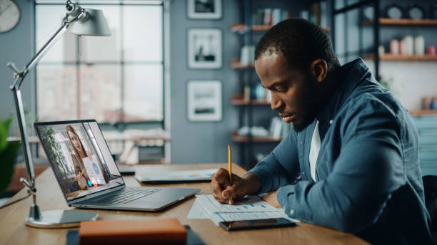istock Handsome African American Man Having a Video Call on Laptop Computer while Sitting Behind Desk in Living Room. Freelancer Working From Home and Talking to Colleagues and Clients Over the Internet. 1311088262