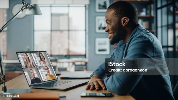 Handsome African American Man Having A Video Call On Laptop Computer While Sitting Behind Desk In Living Room Freelancer Working From Home And Talking To Colleagues And Clients Over The Internet Stock Photo - Download Image Now