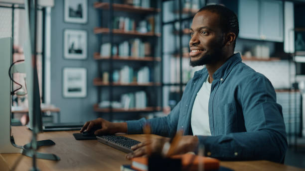 istock Handsome Black African American Specialist Working on Desktop Computer in Creative Home Living Room. Freelance Male is Working on a Finance Presentation Report for Clients and Employer. 1311088352