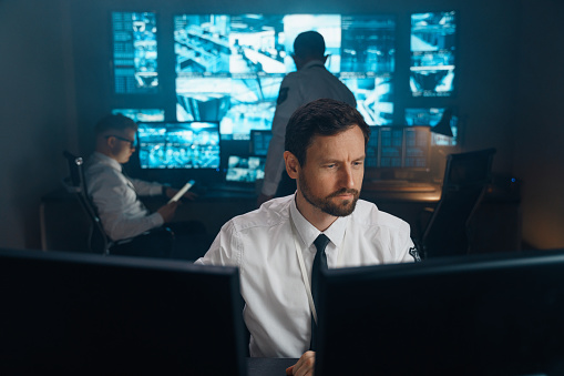 An employee of security, security, police, rescue service, FBI, CIA, sits at his workplace behind monitors. The man works behind two monitors, he studies the received information.