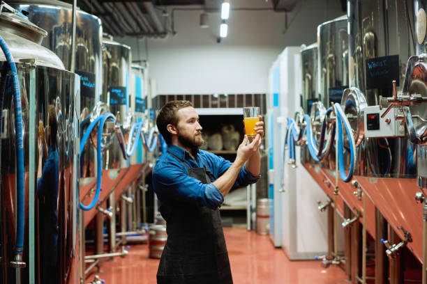 istock Young brewery worker with glass of beer evaluating its visual characteristics after preparation 1311088991
