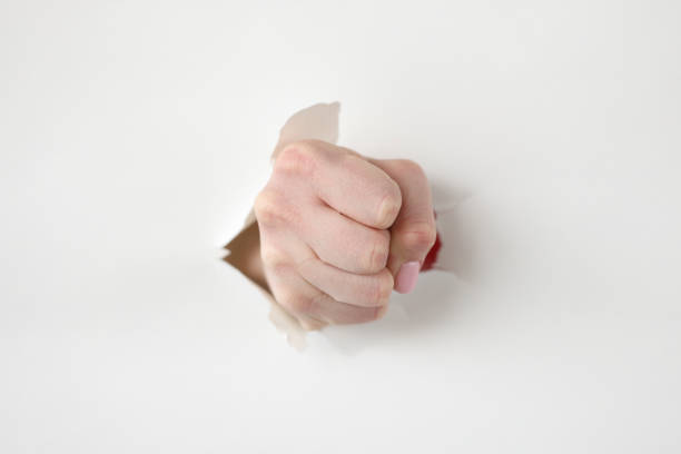 istock Tightly clenched fist through hole in white paper 1311089645