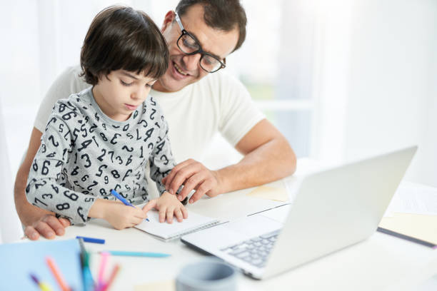 istock Develop a passion for learning. Cute little latin son spending time with his father at home. Businessman using laptop while working from home during lockdown and watching child 1311095595
