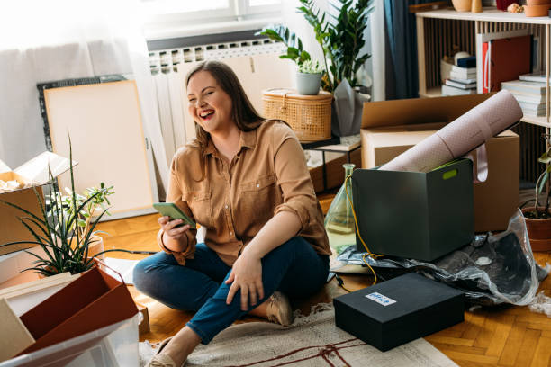 istock Moving In: Beautiful Happy Plus Size Woman Sitting on the Floor while Using a Smartphone (Horizontal) 1311096902