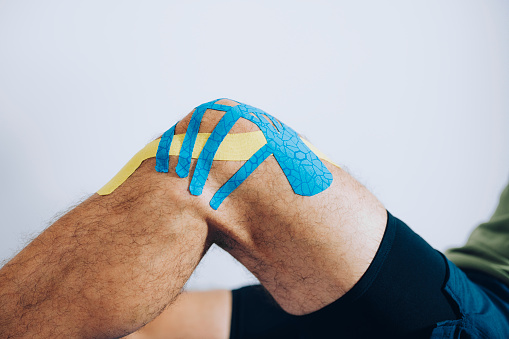 Close up of the knee of male athlete with blue and yellow kinesio tape applied to it