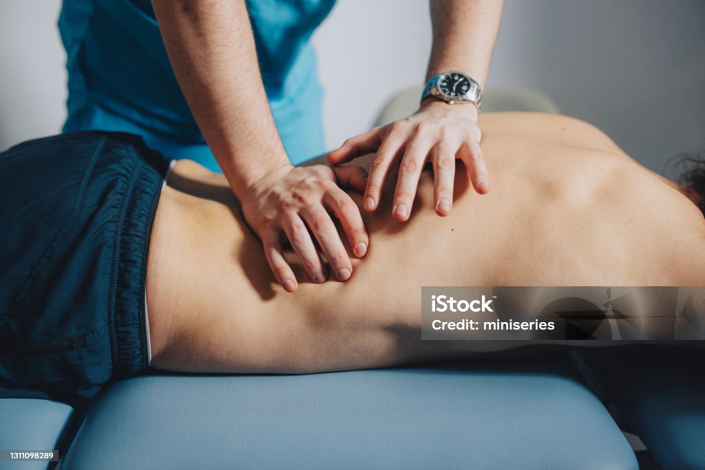 Close up of Physical Therapist Massaging Lower Back Physical therapist is using his hands to massage the lower back of a male patient lying on his stomach. Physical Therapy Stock Photo