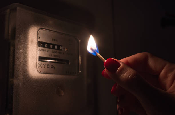istock Hand in complete darkness holds a burning matchstick to reading a home electricity meter. Blackout, energy crisis or power outage, concept image. 1311101287